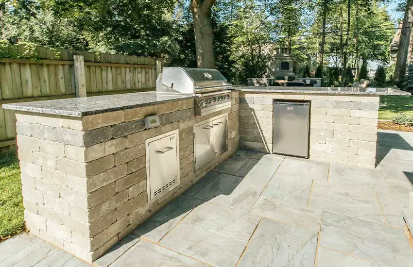 Backyard outdoor kitchen and hardscape installation with stone countertops and built-in appliances