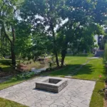 Completed fire pit patio with interlock stone surrounded by mature trees and landscaped lawn in Mississauga