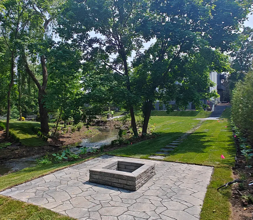 Completed fire pit patio with interlock stone surrounded by mature trees and landscaped lawn in Mississauga