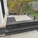 Modern stone porch with large format pavers and glass railing overlooking landscaped backyard in Mississauga