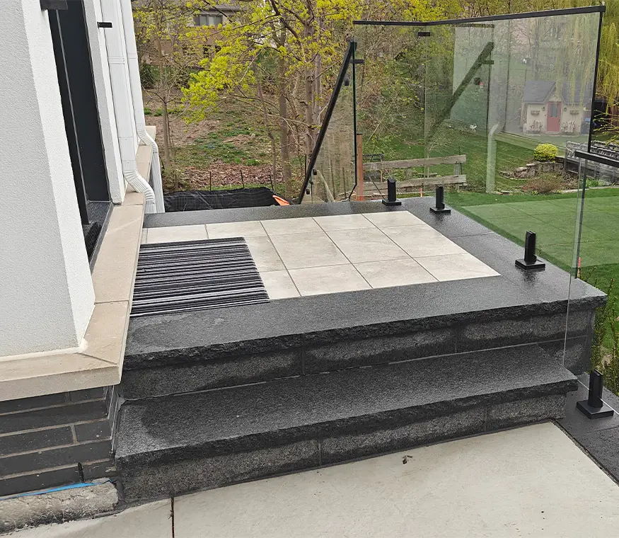 Modern stone porch with large format pavers and glass railing overlooking landscaped backyard in Mississauga