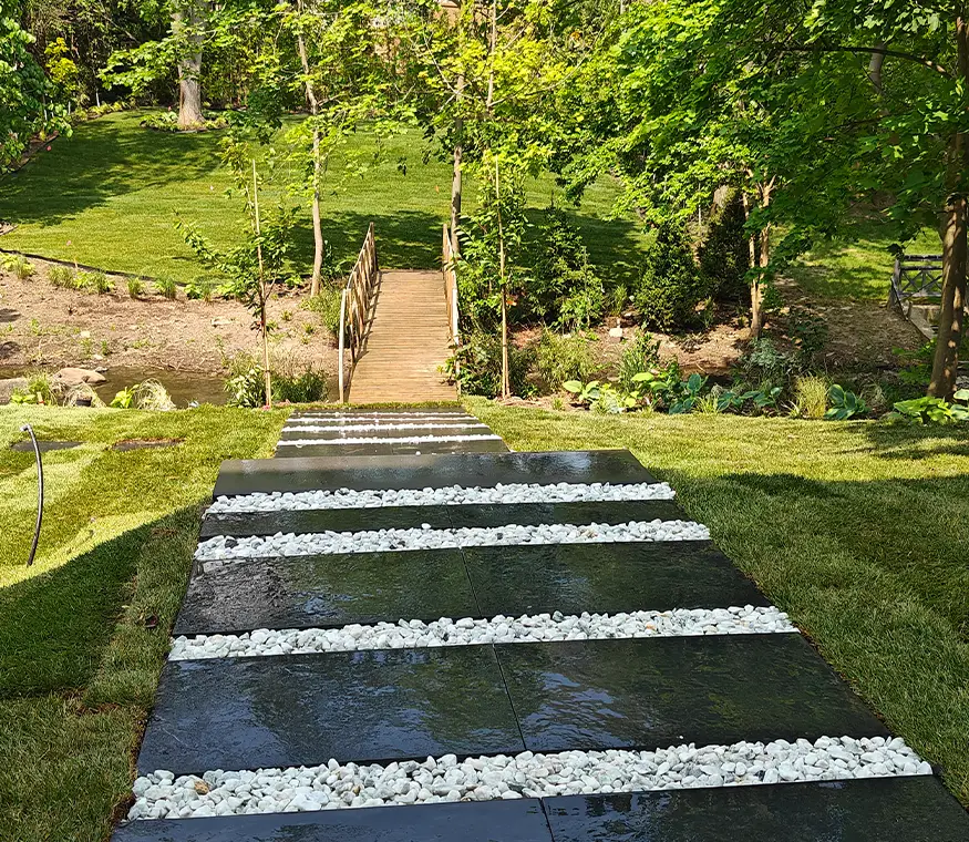Natural stone steps with white decorative gravel strips leading to wooden bridge in landscaped Mississauga backyard