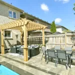 Backyard entertainment space with pergola, outdoor dining area, and stone patio next to a pool