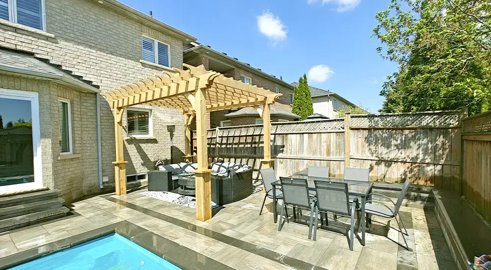 Backyard entertainment space with pergola, outdoor dining area, and stone patio next to a pool