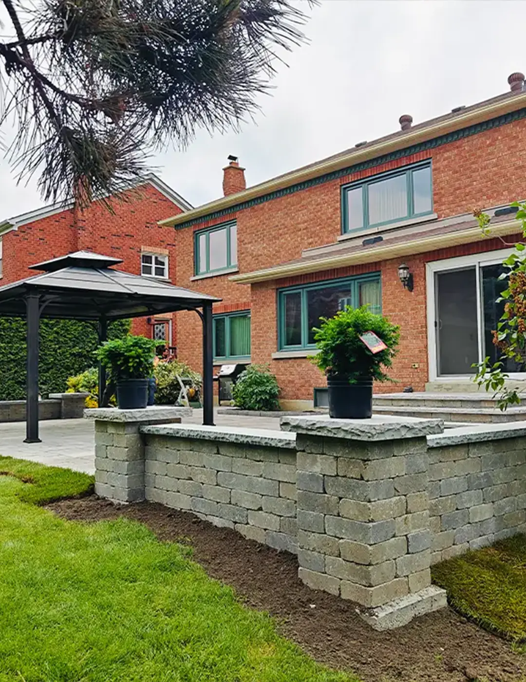 Backyard patio with raised stone seating wall, gazebo, and landscaped garden beside a brick home