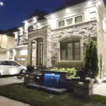 Luxury home exterior with custom stone landscaping and illuminated water feature at the front entrance