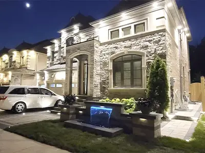 Luxury home exterior with custom stone landscaping and illuminated water feature at the front entrance