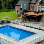 Modern backyard with large in-ground pool, stone patio, and raised deck attached to a residential home
