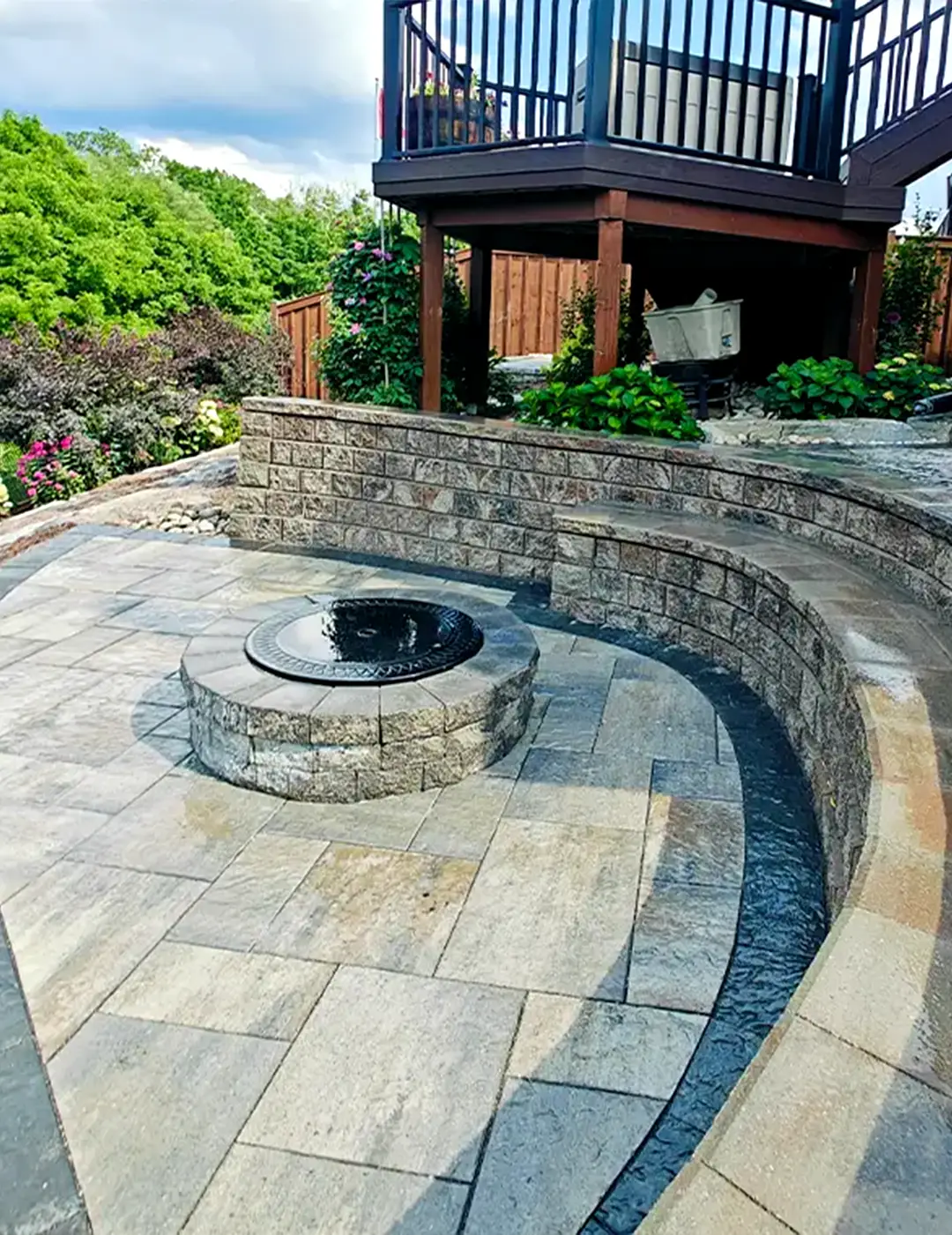Stone patio with curved retaining wall and built-in circular fire pit in a landscaped backyard